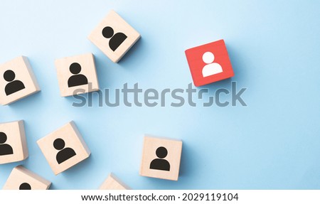 Red wooden cube with person icon stand out from the crowd on blue background. Dissenting opinion, divergent views and different concepts