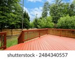 Red Wooden Deck With Wooden Railing Overlooking Fenced Backyard With Trees