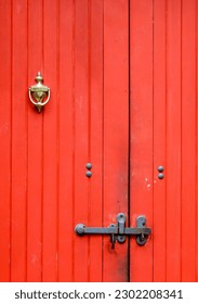Red wooden door with brass knocker and bar latch