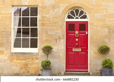 Red Wooden Doors In An Old Traditional English Stone Cottage With Two Plant Pots In Front .