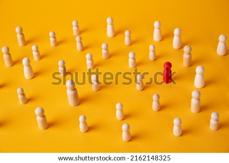 A red wooden figurine of a person is in a crowd of figurines on a yellow background