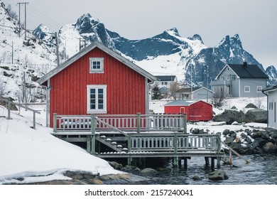 Red wooden fishing cottage rorbuer on coastline surrounded by snowy mountain on winter at Nordland, Lofoten Islands, Norway 