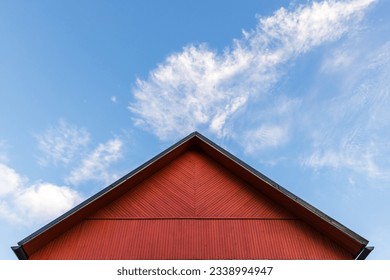 Red wooden gable is under blue cloudy sky on a daytime, rural Scandinavian architecture background