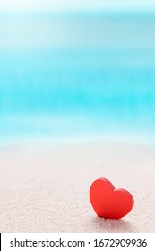 Red Wooden Heart Model On The Sandy Sea Beach With Blue Sea Blurred Background, Vertical View.