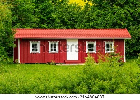 Red wooden house in a nature with a lot of green trees and lawn. Vacation in the country. Wooden hut in the forest 