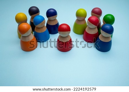A red wooden peg doll surrounded by colorful wooden peg dolls, isolated on blue background. A leadership concept photo. A selective focus photo of the red peg doll.