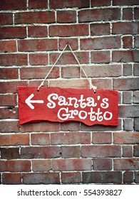 A Red Wooden Sign For A Santa's Grotto On A Brick Wall