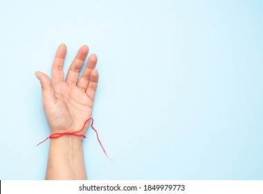 Red Woolen Thread On The Wrist Of A Female Hand, Blue Background, Copy Space