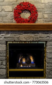 A red wreath on the mantle of a stone fireplace with a Natural Gas brass Fireplace with dancing flames