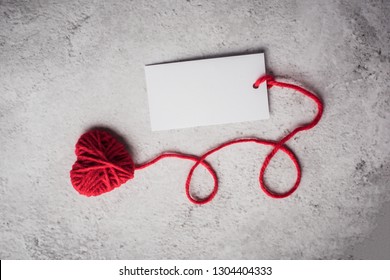 Red Yarn Heart Shaped With White Note Card On The Wall Background