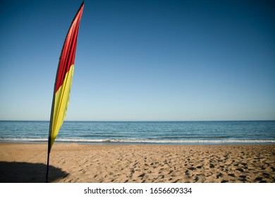 Red And Yellow Beach Safety Flag Against Blue Sky, Fluttering In Wind.