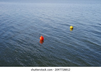 A red and a yellow buoy float on the water.