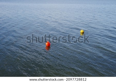 A red and a yellow buoy float on the water.