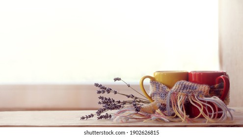 red and yellow cups are wrapped in a purple scarf and decorated with a lavender bouquet against the background of the window. date with the aroma of coffee