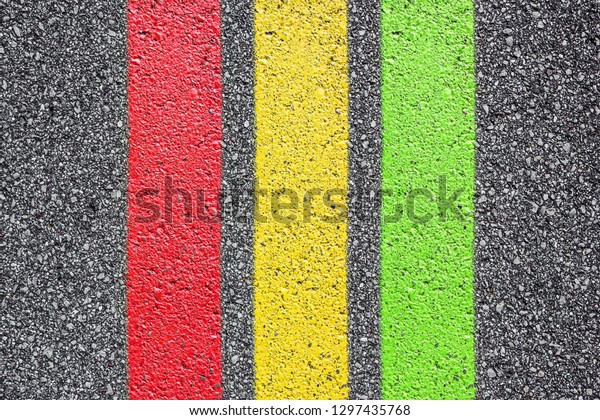 Red, yellow, green paint lines\
on black asphalt. Road texture transportation\
background