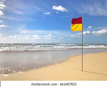 A Red And Yellow Life Saving Flag Against A Blue Sky