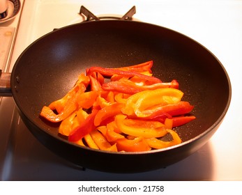 Red, Yellow, and Orange bell peppers, being sauteed in a frying pan.