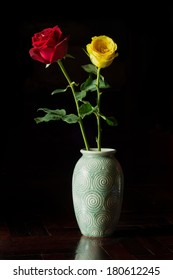 red and yellow roses in vase on black background.