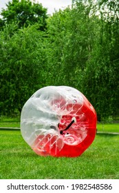 Red Zorbing Balloon on the summer lawn. Inflatable zorb ball outdoor. Leisure activity concept with vertical copy space.