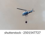 REDDING CALIFORNIA – AUGUST 10, 2024 –A Bell UH-1 helicopter with a full load of water from Mary Lake flying into the smoke of the Lower Fire near Lower Springs and Keswick.