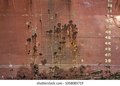 Reddish brown ship hull with stains of rusty and yellow numbers