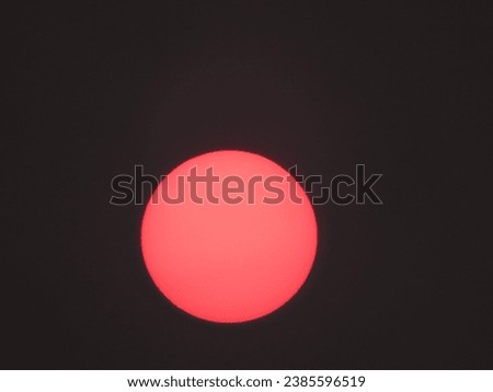 reddish sun, with its perfect circular shape, in the darkened sky due to its luminosity