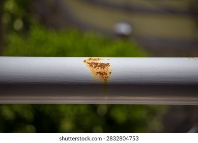 Reddish-brown rust breaking through the painted coating of a horizontal metal balcony railing