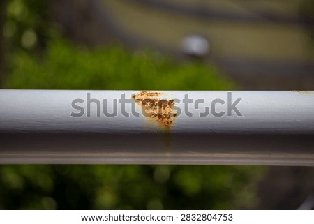 Reddish-brown rust breaking through the painted coating of a horizontal metal balcony railing