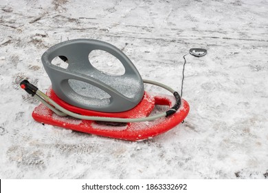 Red-gray Plastic Snow Sled On The Snow On The Road