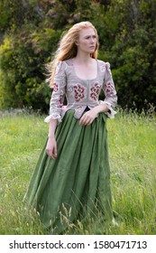 Red-haired 18th Century Woman Wearing An Embroidered Bodice And Wandering In Long Grass