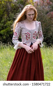 Red-haired 18th Century Woman Wearing An Embroidered Bodice And Wandering In Long Grass