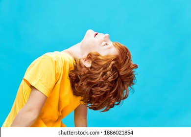 Red-haired boy with his head thrown back looks up blue background 
