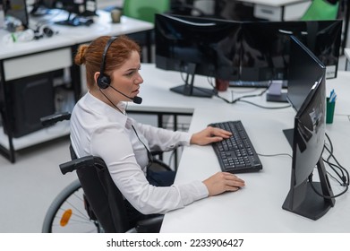 Red-haired caucasian woman in a wheelchair talking on a headset. Female call center worker at her desk. - Shutterstock ID 2233906427