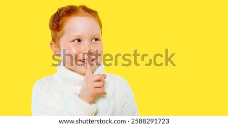 Red-haired child smiles playfully while making shushing gesture against bright yellow background