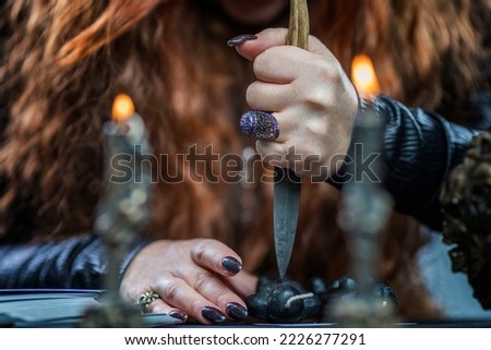 A red-haired female witch performs a magical ritual with a knife and a voodoo doll by burning candles. Occultism and mysticism. Close-up.