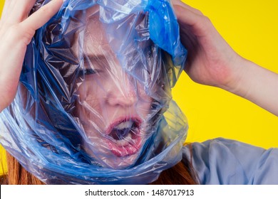 redhaired ginger european woman suffocation head in blue polyethylene package in studio yellow background. eco pollution cellophane film concept.