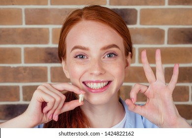 redhaired ginger female with snow-white smile holding white wisdom tooth after surgery removal of a tooth - Shutterstock ID 1424822162