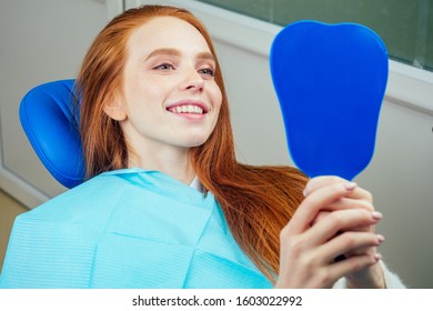 redhaired ginger lady checking teeth in mirror at dentist office