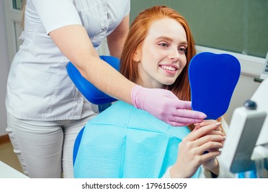 redhaired ginger lady checking teeth in mirror at dentist office