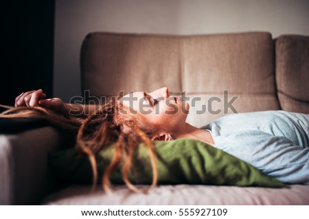 red-haired girl with dreadlocks lying on the couch at home with eyes closed