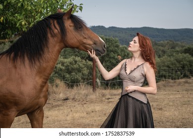 a red-haired girl feeds a brown horse and talks to it