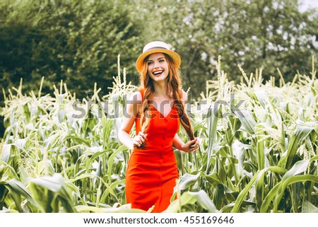 
red-haired girl with freckles in red dress walking on a field of corn she is smiling a sweet smile on her head Summer panama