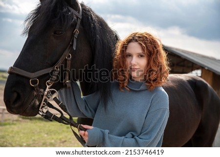 A red-haired girl holds a horse by the bridle.