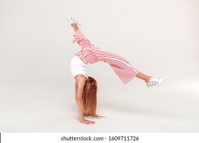 Red-haired girl isolated on grey background inclusive beauty standing on hands doing front handspring