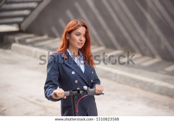 A red-haired girl in a jacket and trousers drives an\
electric scooter along the wall. A business woman in a pantsuit and\
red high heels rides around the city in a modern car. Office\
worker. Dress code