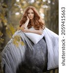 Red-haired girl on a gray horse under a blanket in the autumn forest