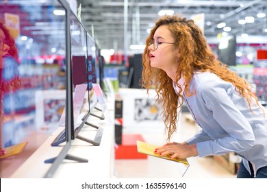 Red-haired Girl Shopper Standing Close In Front Of A New TV In An Electronics Store