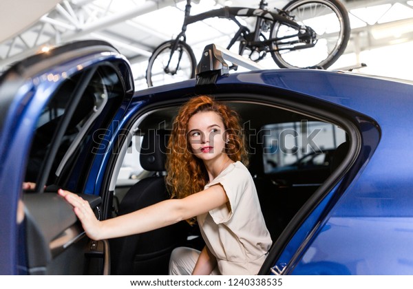 Red-haired girl sitting in a car with bicycles on\
the roof