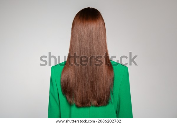 Red-haired girl with straight long hair. Back\
view. Gray\
background.