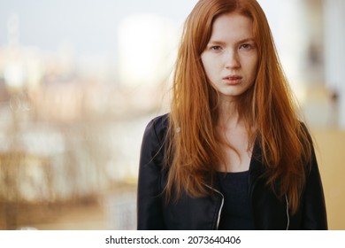 a red-haired girl without makeup looks seriously against the blurred background